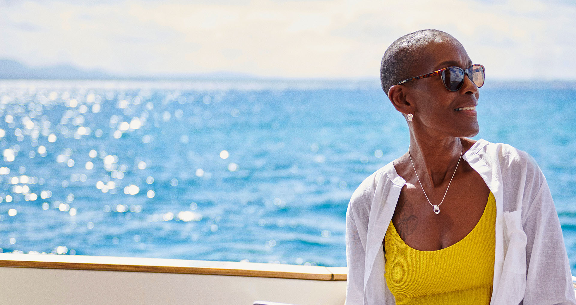 Woman sitting on a yacht in summer clothes, gazing into the distance and smiling. 