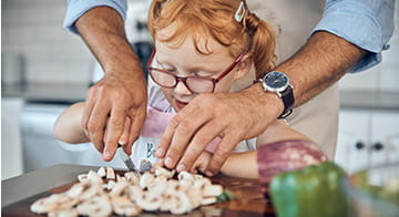 Young girl having a cooking lesson with a relative and being helped to chop vegetables