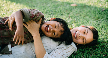 Child and mother laying on grass, playing and smiling