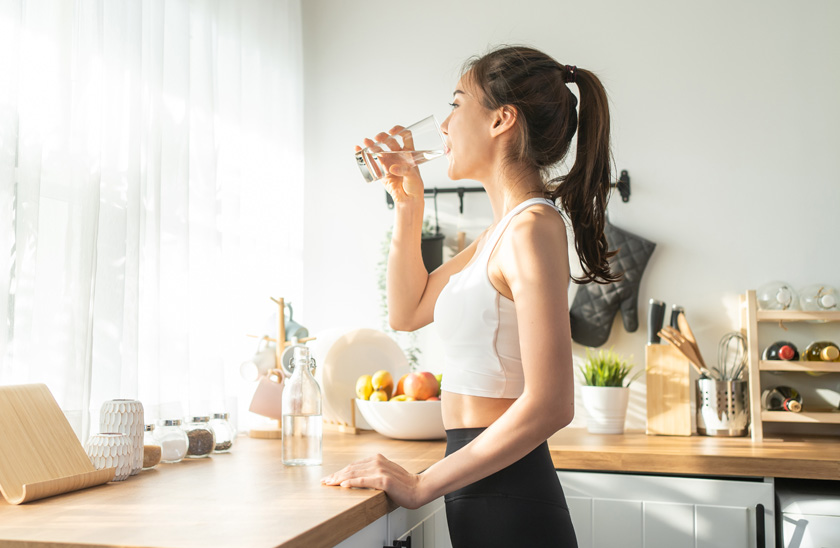 woman in gym clothes drinking water in a sunny kitchen