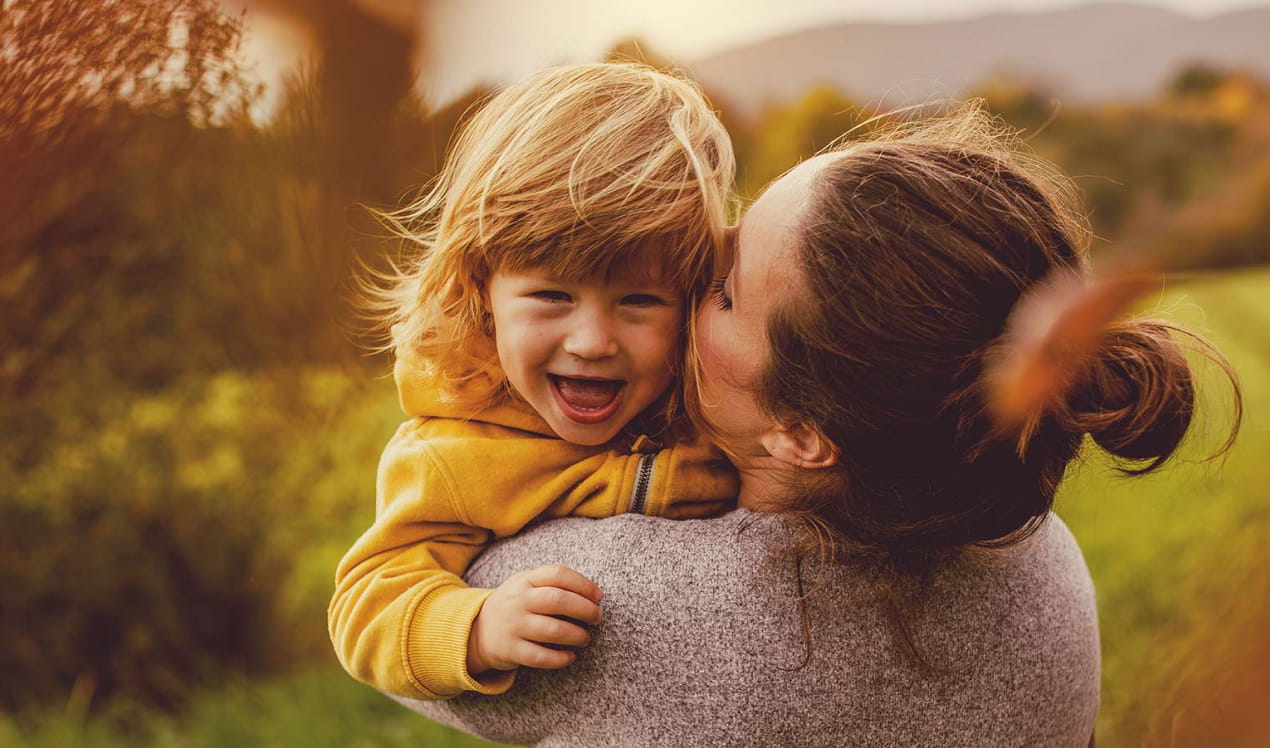 Mother hugging happy child with green fields in background