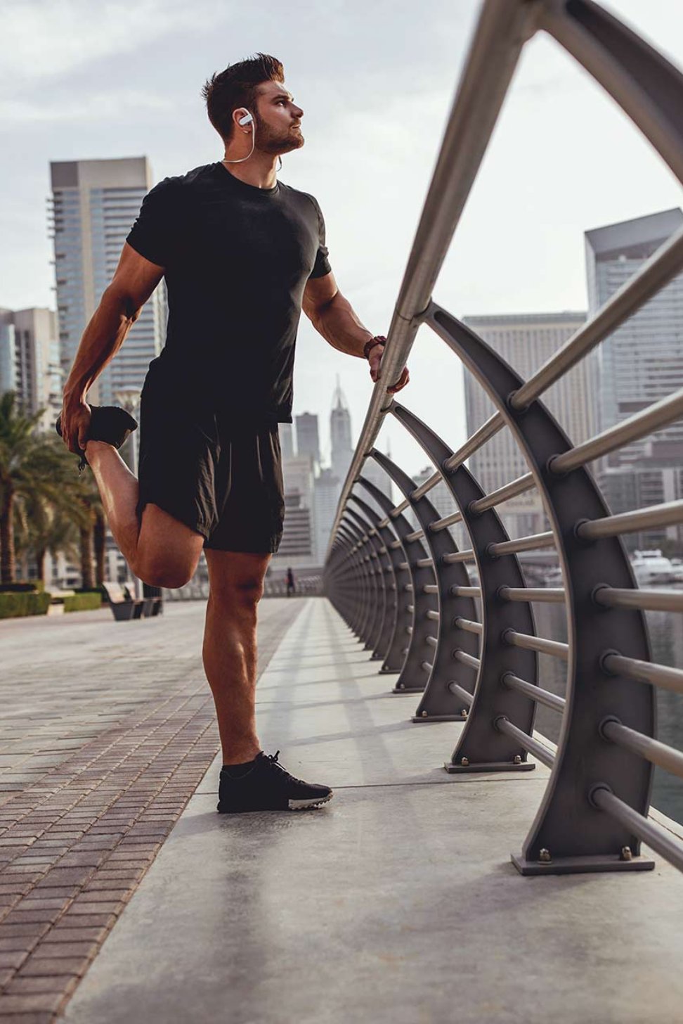 man in gym clothes stretching leg outside in city