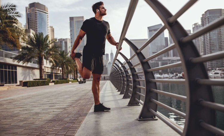 man in gym clothes stretching leg outside in city
