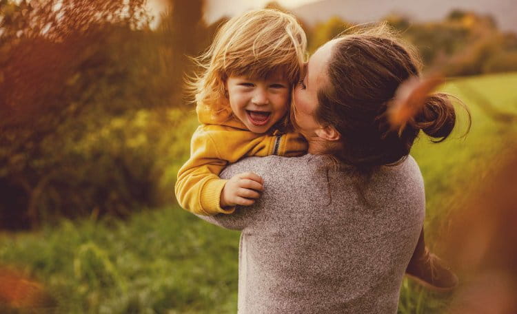 Mother hugging happy child with green fields in background