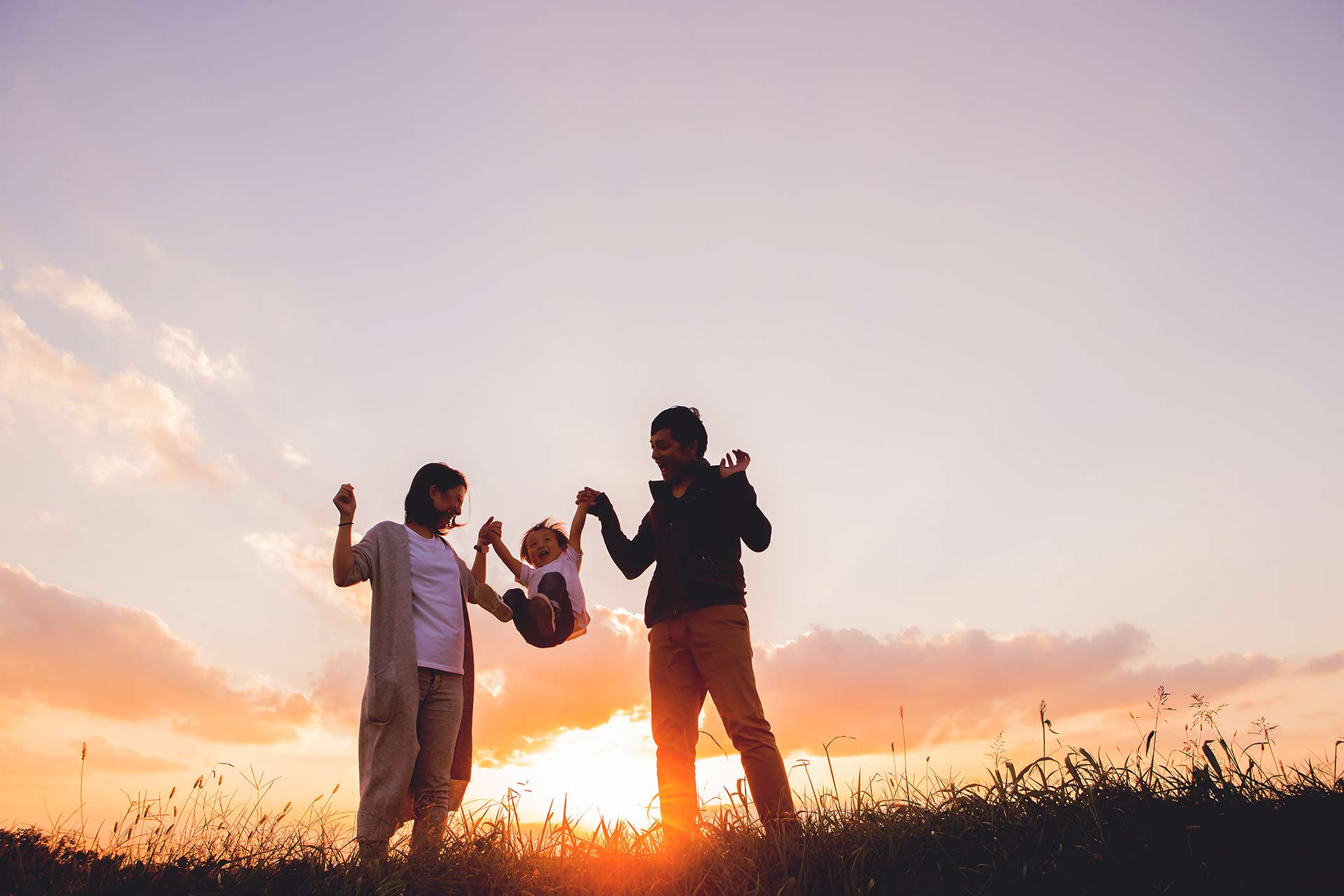 , image shows family swinging a child with a sunset in the backgroun