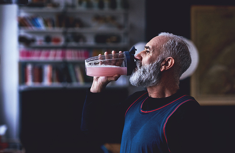 Man with grey hair and beard in gym clothes drinking smoothie