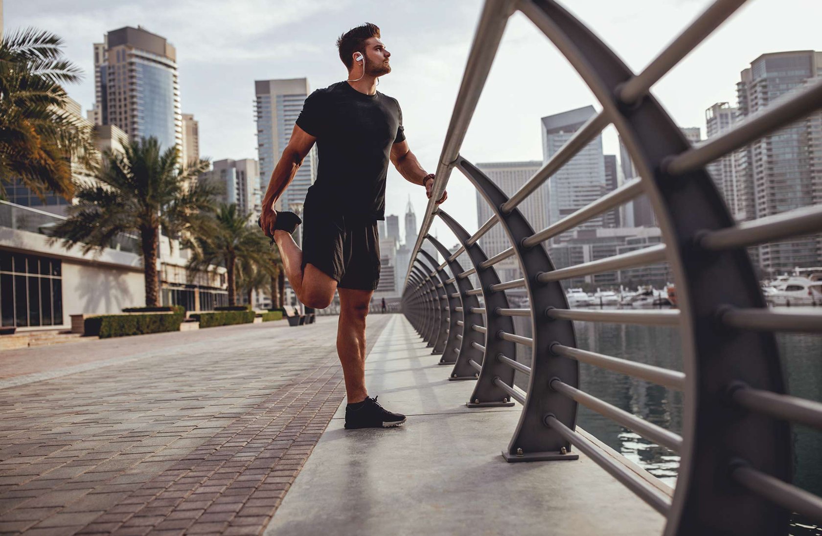 man in gym clothes stretching leg outside in city